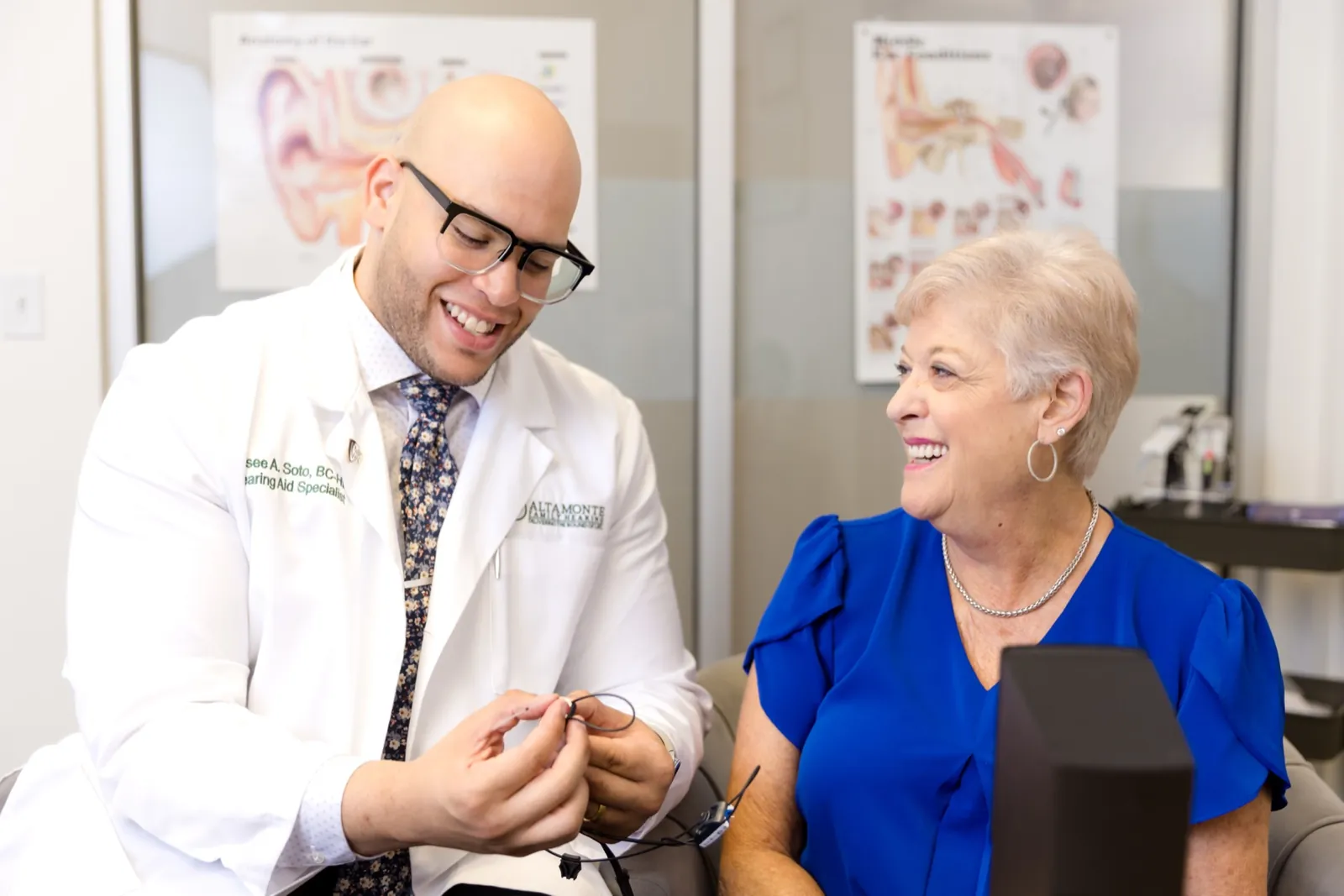 Jaysee showing a patient her new hearing aid, both of them smiling
