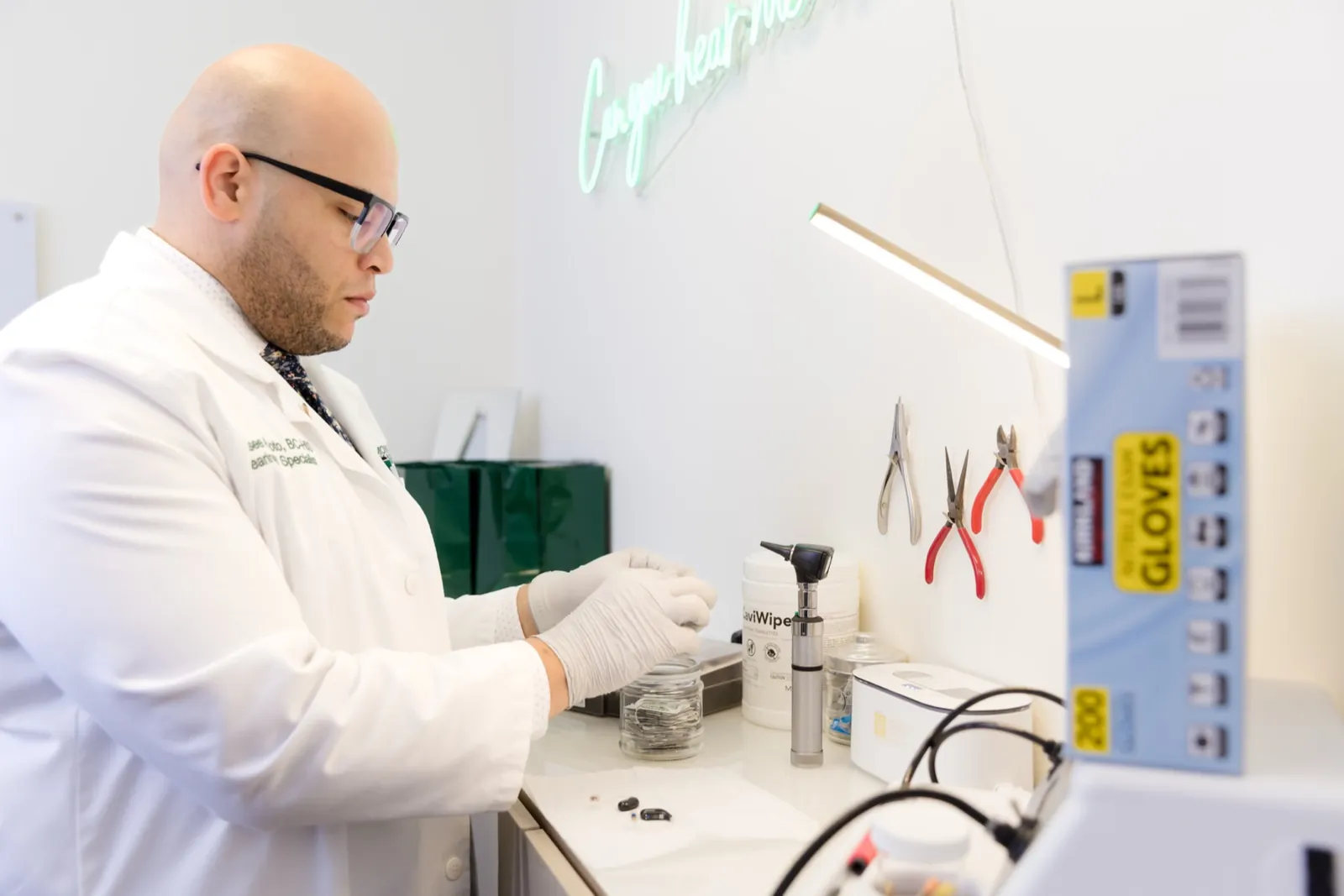 Jaysee at the repair bench cleaning a hearing aid