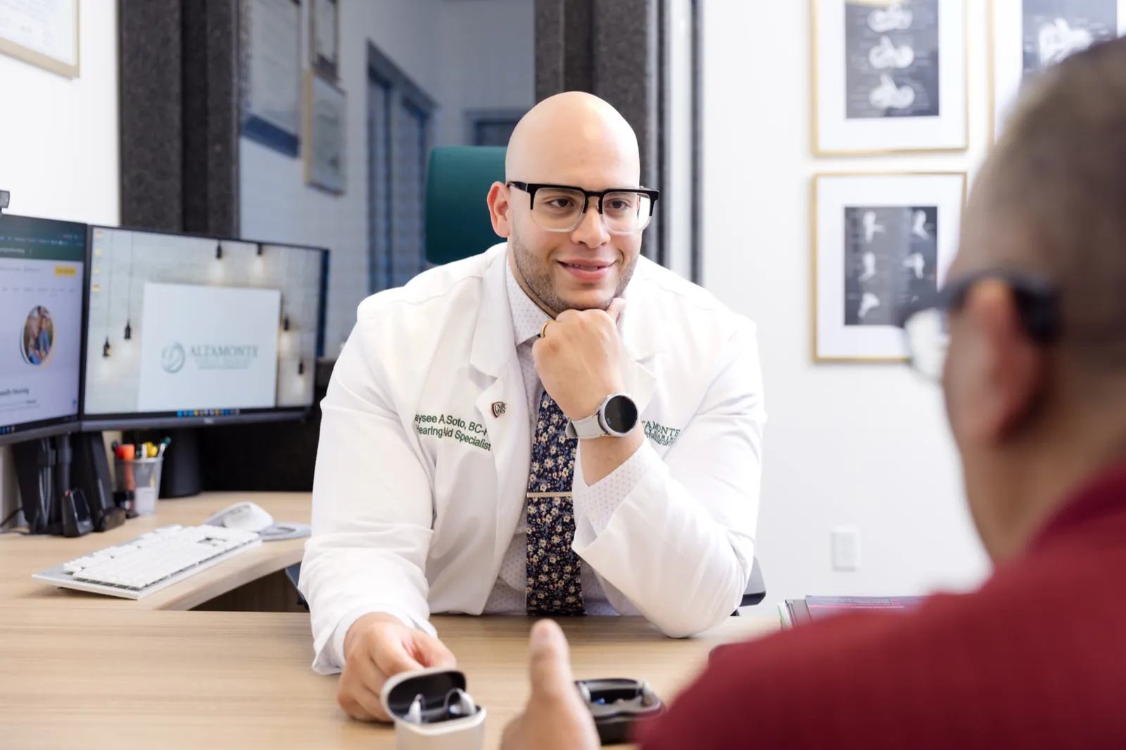 Jaysee explaining hearing aid features to a patient across his desk