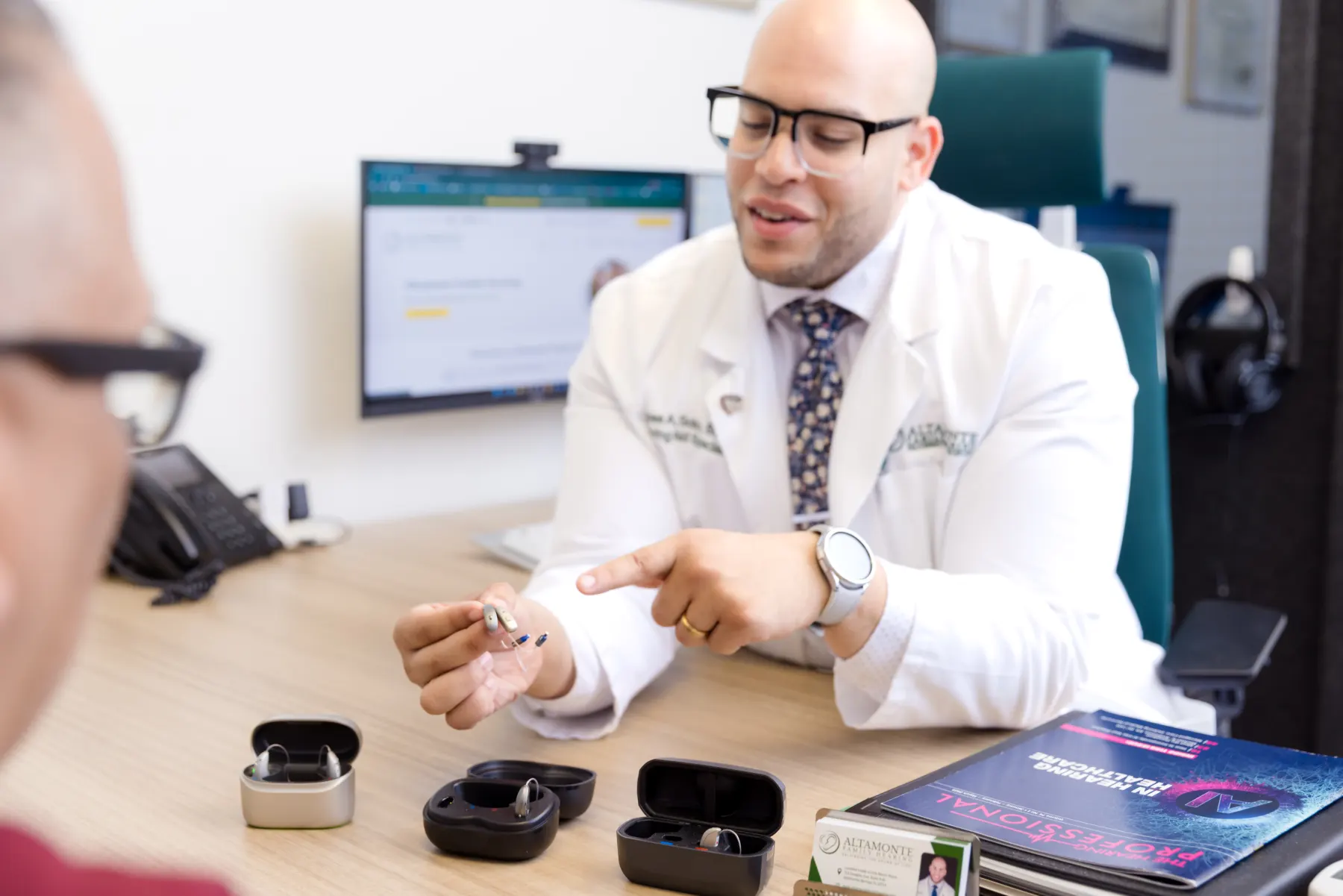 Jaysee showing a patient hearing aids and their cases across his desk