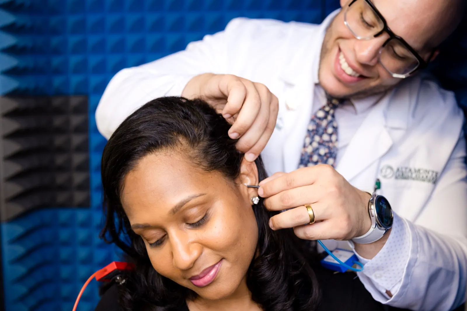 Jaysee placing an earpiece in a patient's ear in the sound booth