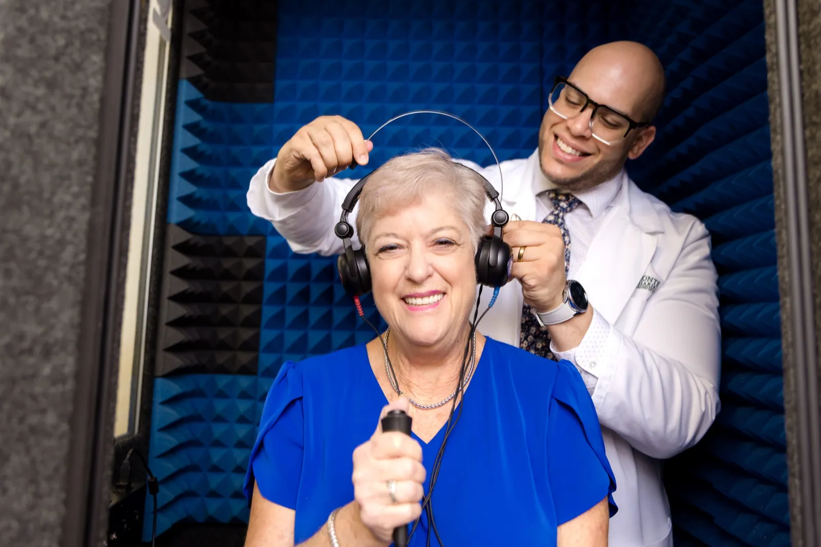 Jaysee placing headphones on a smiling patient in the sound booth